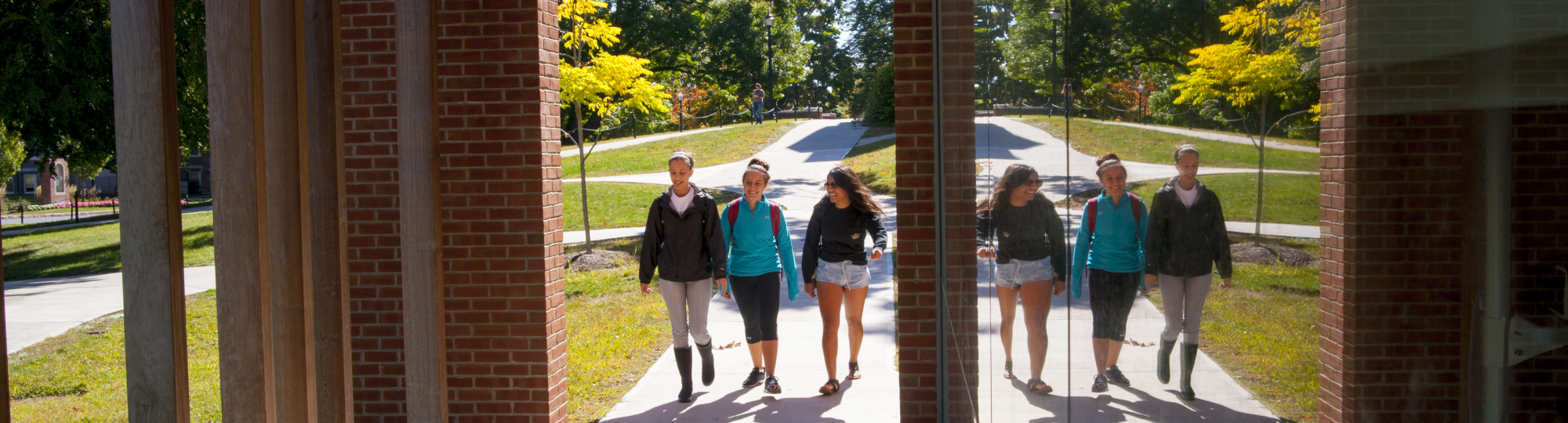 Three students walk under the front portico of Storrs Hal