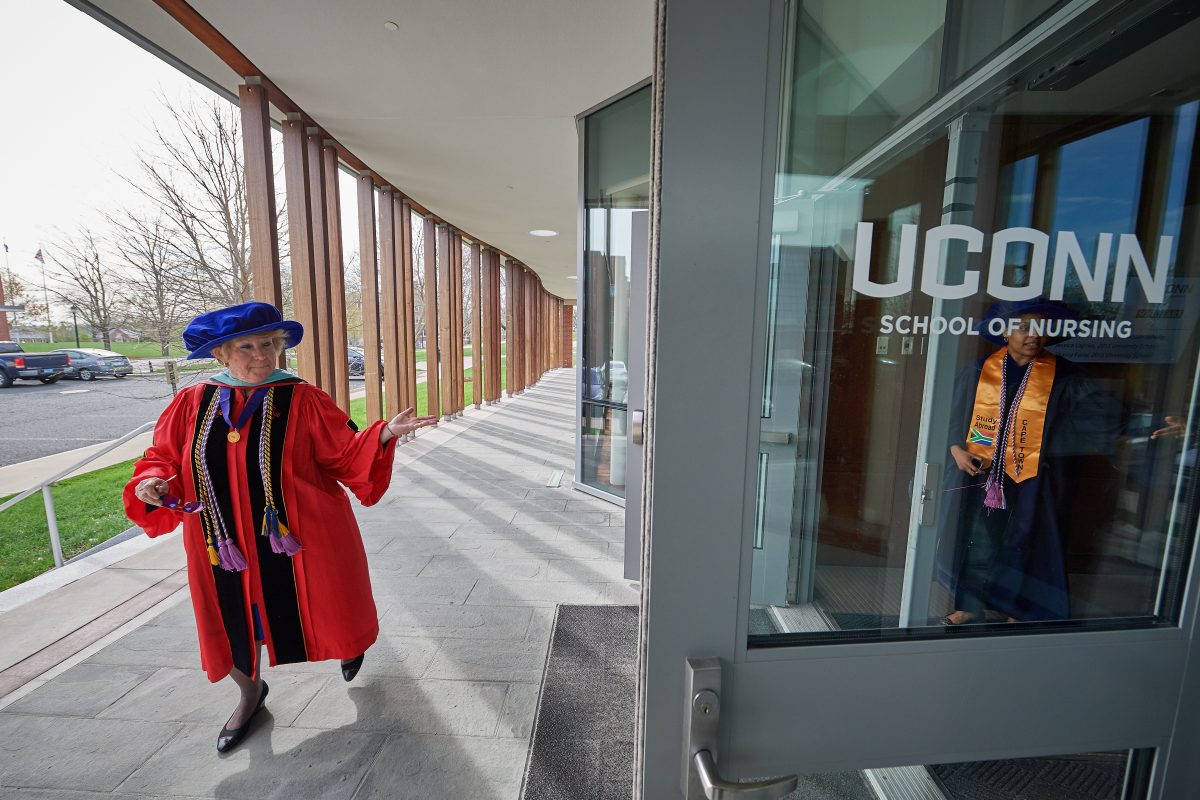 A faculty member in regalia gestures to students in graduation robes..