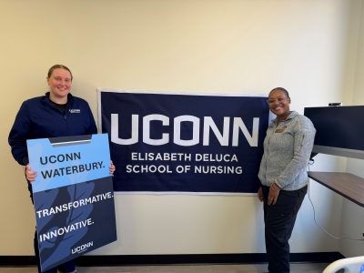 A UConn Waterbury student and Nursing faculty member show their pride for Nursing in Waterbury by holding campus and school signs.