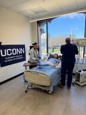 UConn Waterbury student and their professor practice setting up an IV on a mannequin. 